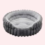 Lit avec matelas amovible pour chat de forme ronde et de couleur grise en peluche sur fond rose.