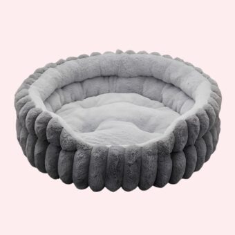 Lit avec matelas amovible pour chat de forme ronde et de couleur grise en peluche sur fond rose.