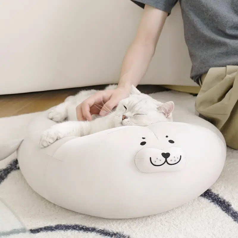 Coussin en peluche en forme de phoque pour chat blanc, confortable sur un tapis dans une maison
