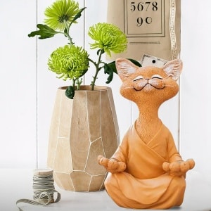 Statuette d'un chat qui médite. L'apparence fait penser à un dessin animé. Le chat est roux avec une tunique orange. Il est en position du Bouodha.