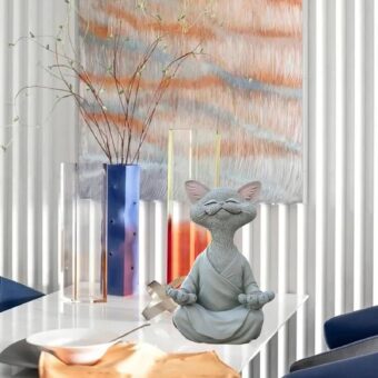 Statuette d'un chat qui médite. L'apparence fait penser à un dessin animé. Le chat est roux avec une tunique orange. Il est en position du Bouodha.
