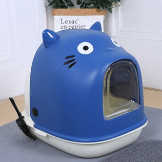 Un bac à litière bleu en forme de chat, il est fermé par une chatière transparente. Il y a une pelle à litière