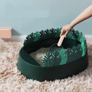Il y a un bac à litière vert orné de feuilles en plastique verte sur les cotés. le bac est posé sur un sol avec moquette et est rempli de litière 