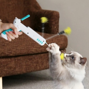 Jouet pistolet avec balles à plumes pour chat, très haute qualité, jouer par un chat devant un canapé dans une maison