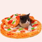 chat noir et blanc se trouvant sur un couchage pour chat représentant un visuel d'une pizza , et par dessus lui, un couverture dans le même motif