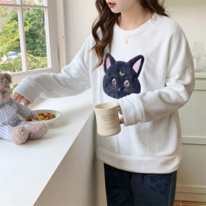 jeune femme brune en train de boire son café, debout dans cuisine, on ne voit pas tête, elle porte une pyjama de chat, dont le pantalon est noir et le pull est blanc avec une tête de chat noir en son centre