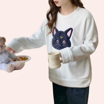 jeune femme brune en train de boire son café, debout dans cuisine, on ne voit pas tête, elle porte une pyjama de chat, dont le pantalon est noir et le pull est blanc avec une tête de chat noir en son centre