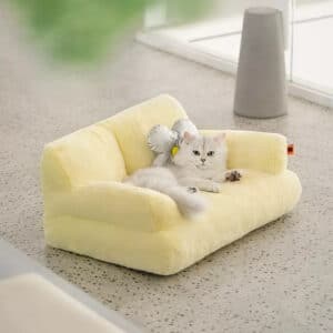 Lit pour chat moderne en fourrure de couleur jaune, posé sur un sol gris avec un chat allongé à l'intérieur