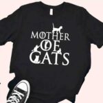T-shirt noir avec écrit Mother of cats en blanc et des dessins de chats qui sont entre et sur les lettres