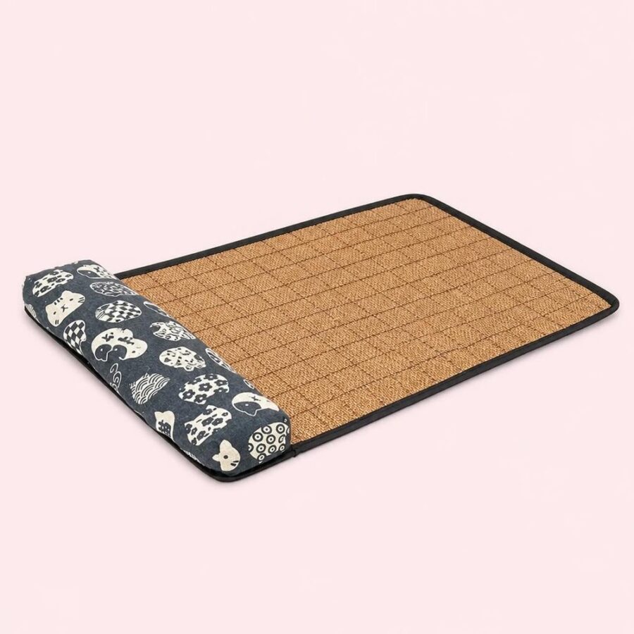 Un tapis rafraichissant chat orné de têtes de chats japonais, avec une surface tissée beige et un côté gris imprimé de chats, posé sur un fond rose clair.